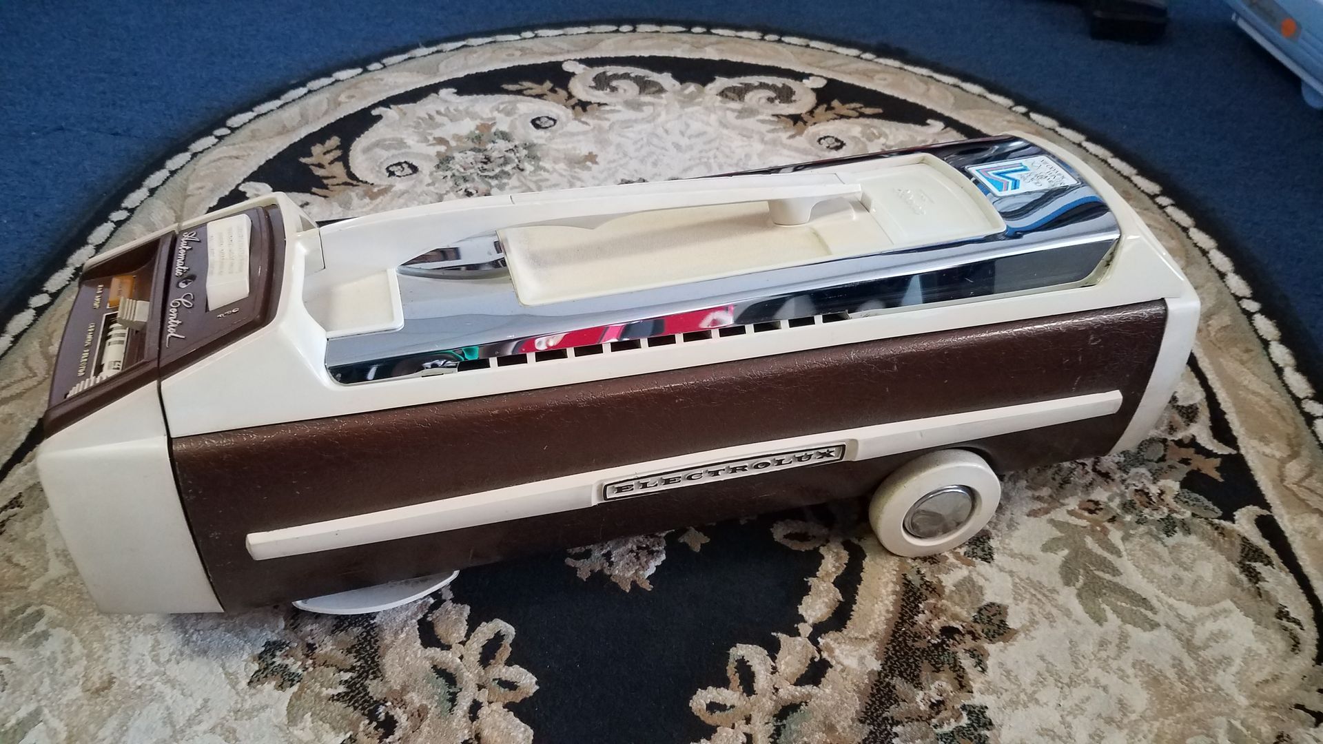Vintage brown-and-cream vacuum cleaner lying on a patterned rug