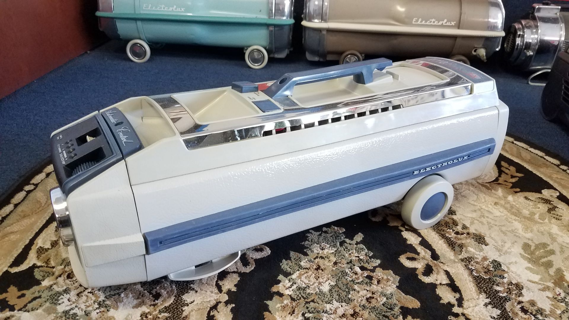 Toy futuristic car with white and blue body, clear roof, and large blue wheels on a patterned rug.
