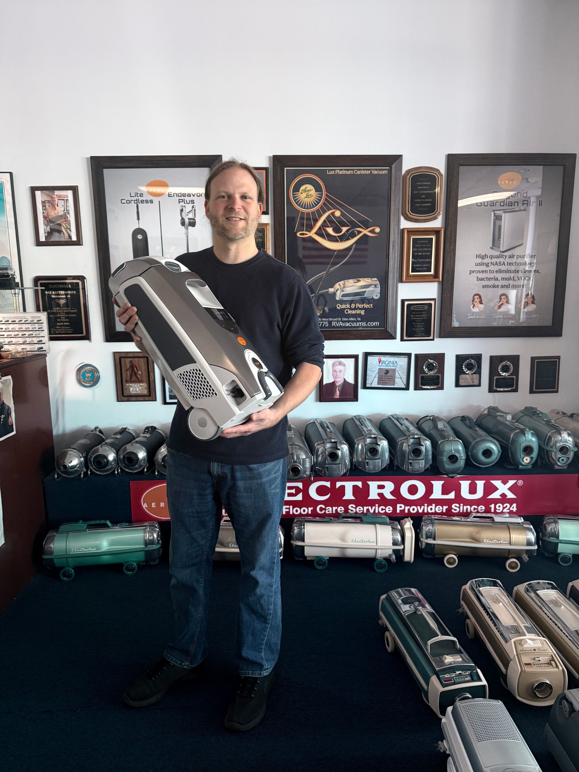Man holding a large silver cylindrical object in a room with vintage industrial displays and framed posters