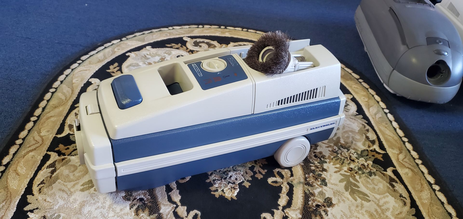 Blue-and-white toy bus on a patterned rug beside a gray computer mouse