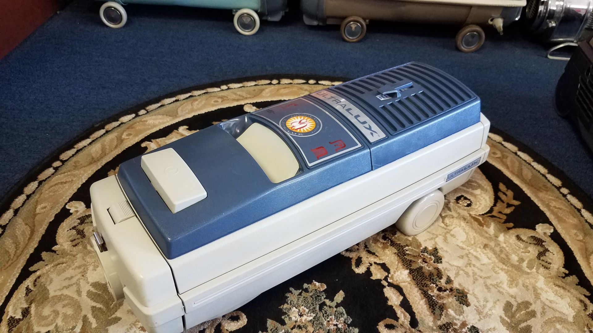 White-and-blue vacuum cleaner on a patterned rug in a living room