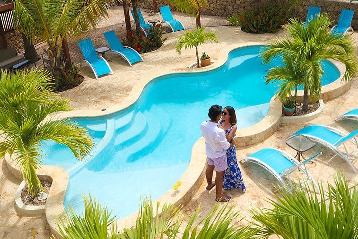 Couple embracing beside a turquoise resort pool with palm trees and lounge chairs
