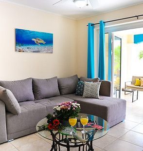 Bright living room with gray sectional sofa, glass coffee table, turquoise curtains, and ocean wall art