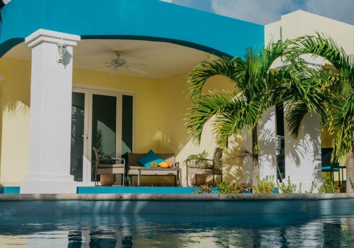 Modern villa patio with turquoise pool, yellow walls, white columns, and palm trees