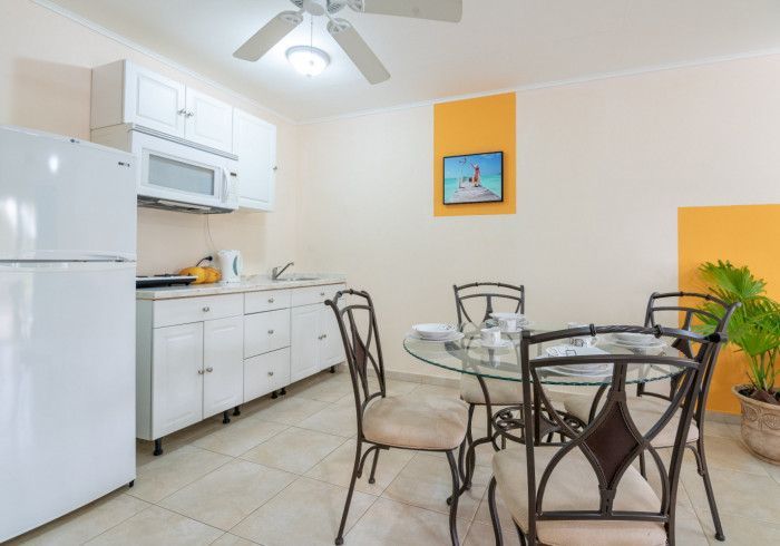 Bright kitchen-dining area with white cabinets, glass table, metal chairs, and orange accent wall.
