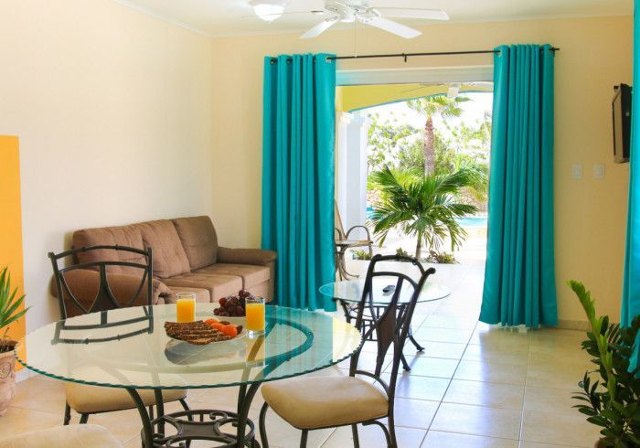 Bright living room with sofa, glass dining table, and open turquoise curtains to a sunny patio.