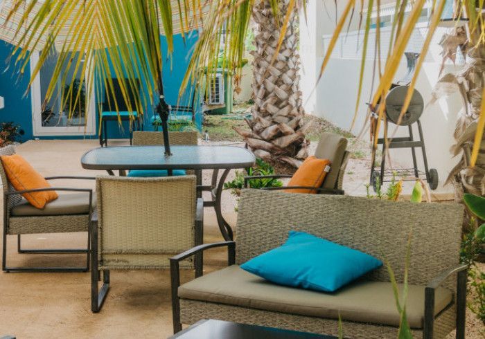 Patio seating area with wicker chairs, turquoise cushions, and a round table beside a palm tree