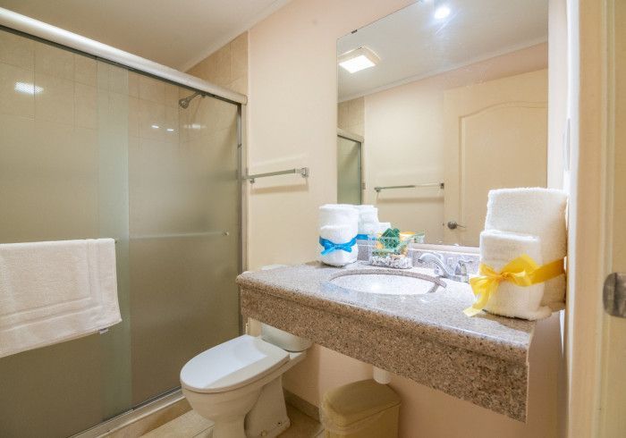 Modern bathroom with glass shower, toilet, granite sink, and neatly folded towels.