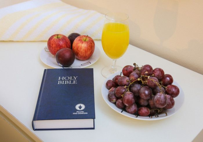 Bible, fruit, and a glass of orange juice arranged on a white table