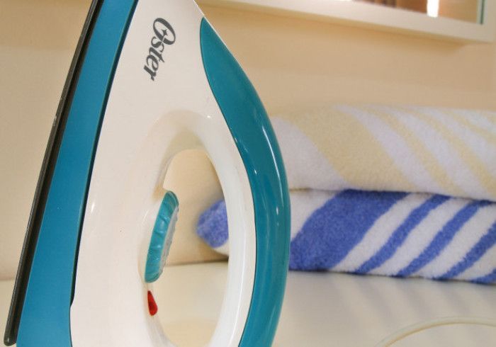 Close-up of a teal and white iron beside a striped folded towel on a bed