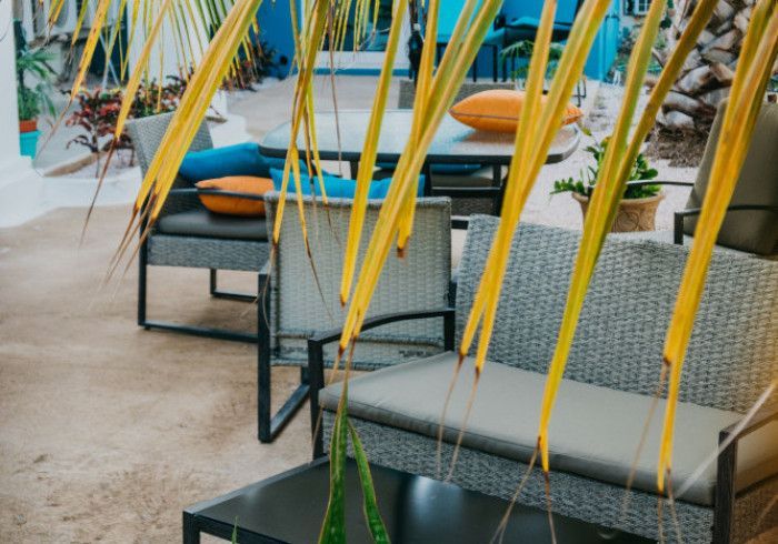 Modern outdoor patio with wicker lounge chairs, orange cushions, and yellow plant leaves in the foreground