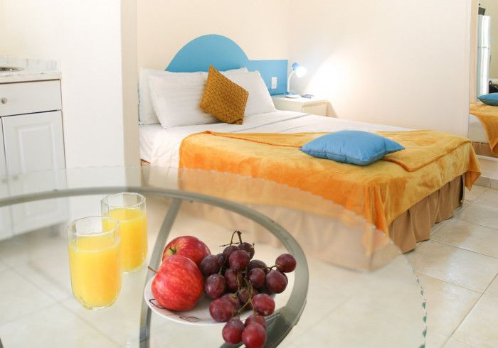 Bright bedroom with a bed, blue and orange bedding, and a glass table with orange juice and fruit