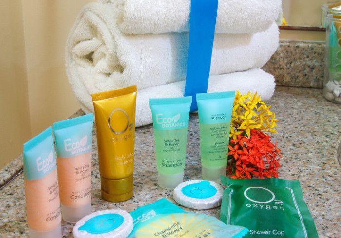 Spa toiletries arranged on a countertop beside rolled white towels and a small red-yellow flower arrangement.