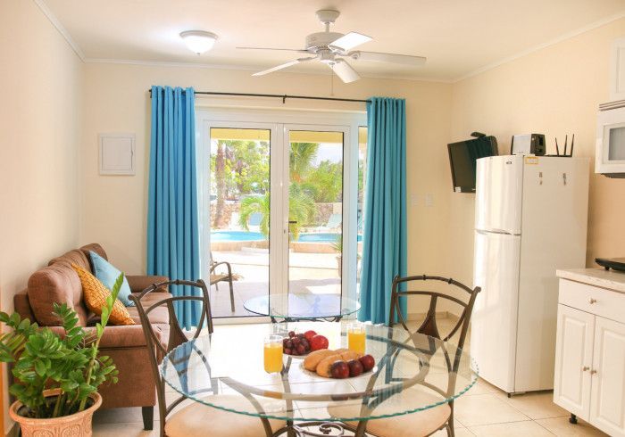 Bright living room with blue curtains, glass table, sofa, and patio doors to a pool.