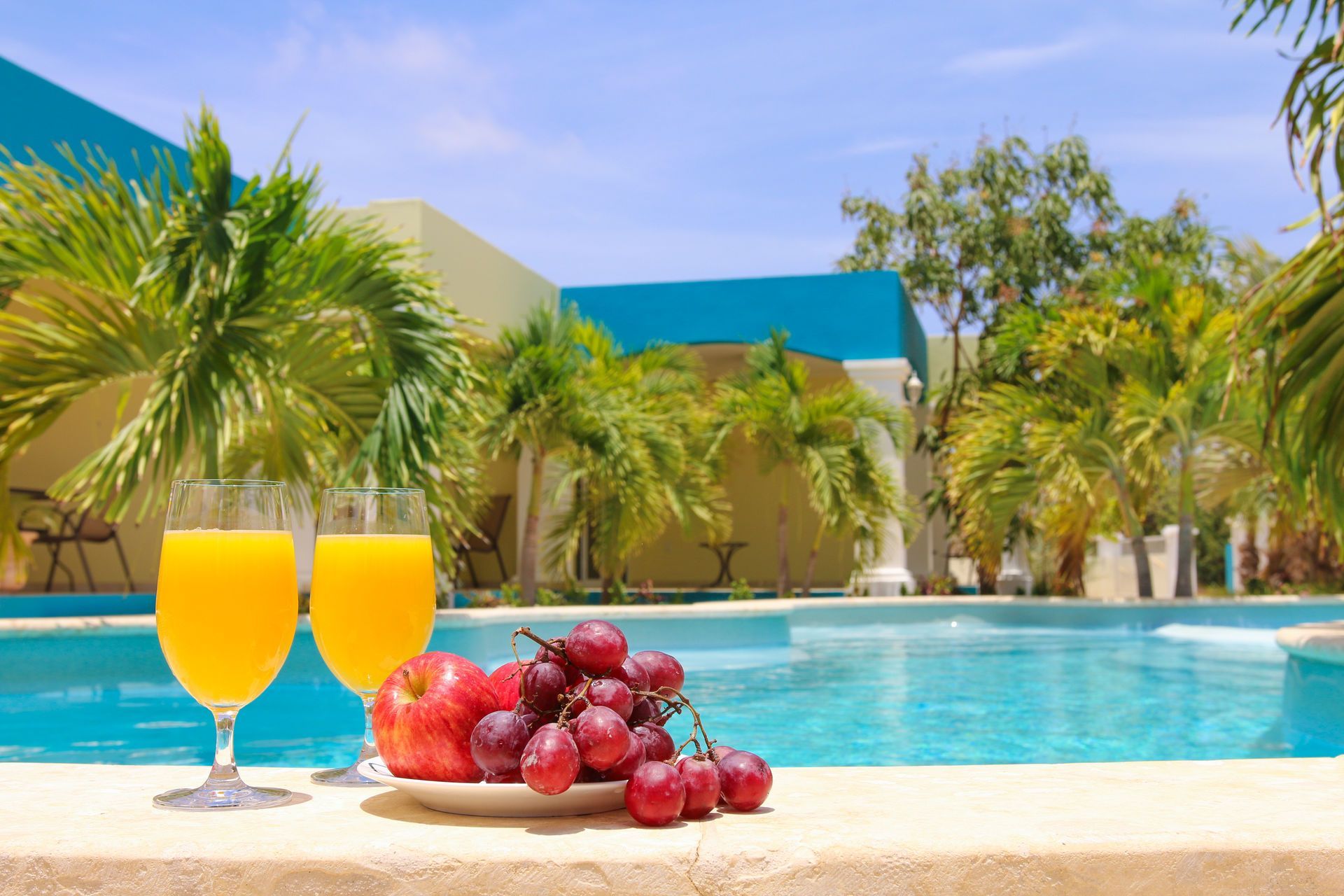 Two orange drinks and grapes by a sunny resort pool with palm trees