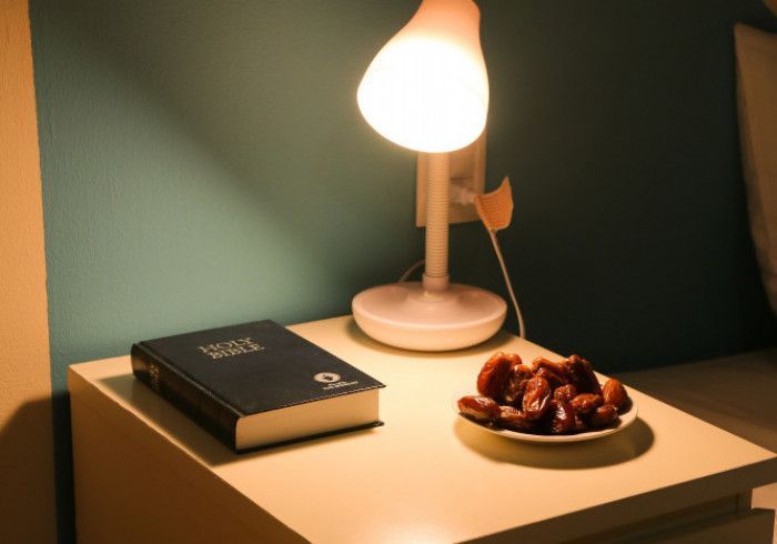Bedside table with a lit lamp, black book, and bowl of snacks in a dim room