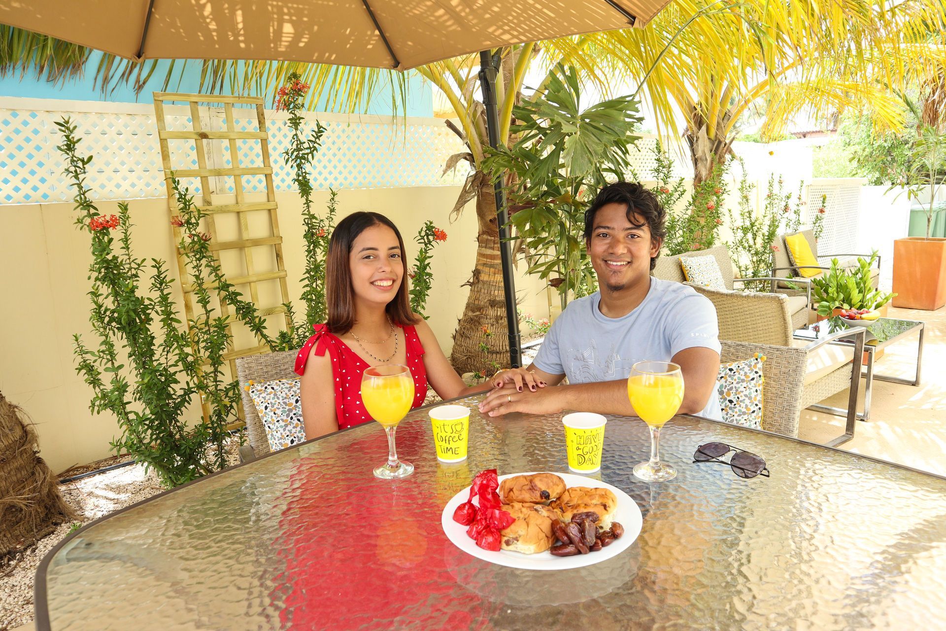 Two people seated at an outdoor café table with drinks and a dessert plate under a patio umbrella