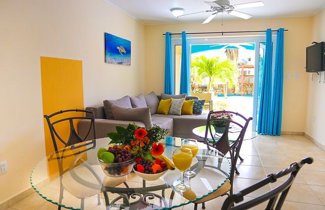 Bright dining area with glass table, tropical flowers, and open patio doors to a sunny pool outside