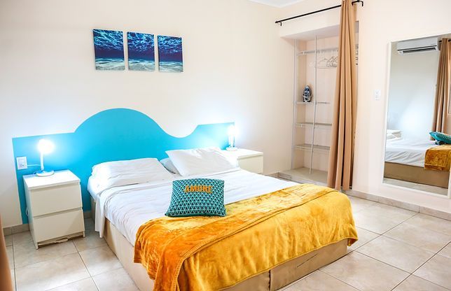 Bright white bedroom with blue headboard, twin beds, yellow blanket, and mirror wardrobe