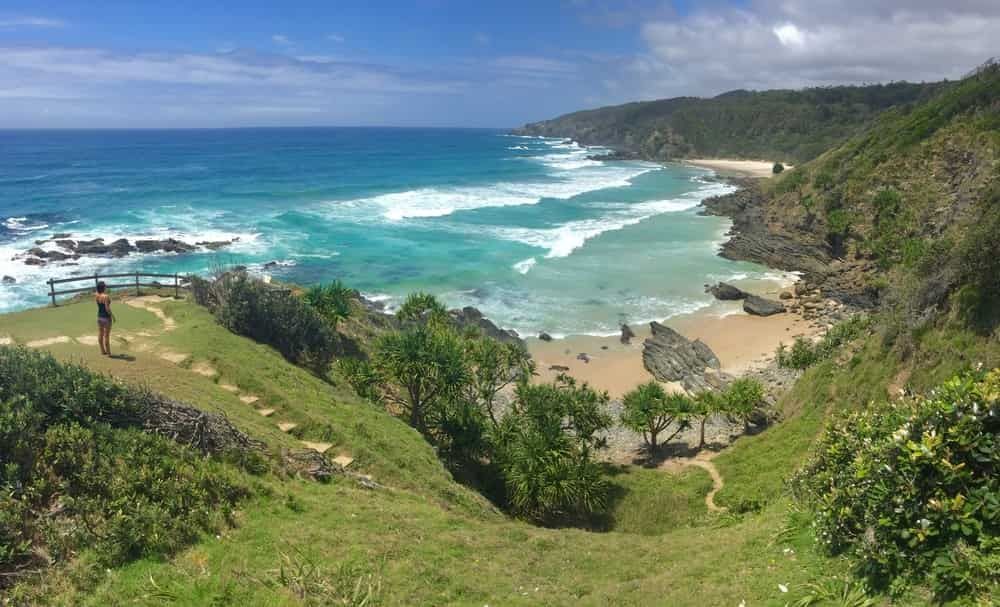 A Person is Standing on a Cliff Overlooking a Beach — AH Electrical in Byron Bay, NSW