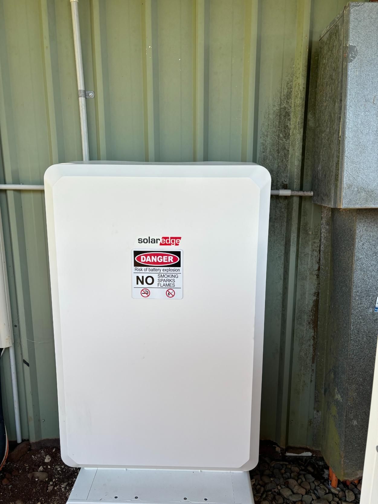 A White Box With A Danger Sign On It Is Sitting Next To A Green Wall — AH Electrical in Ballina, NSW