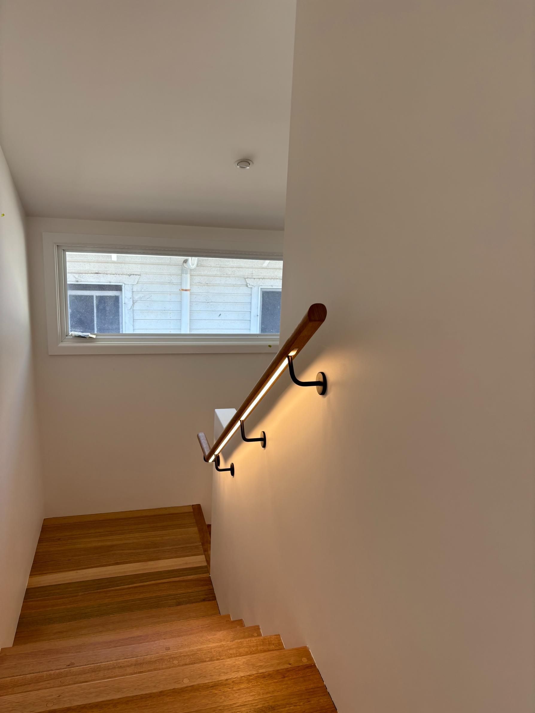 A Wooden Staircase With A Wooden Railing And A Window — AH Electrical in Byron Bay, NSW
