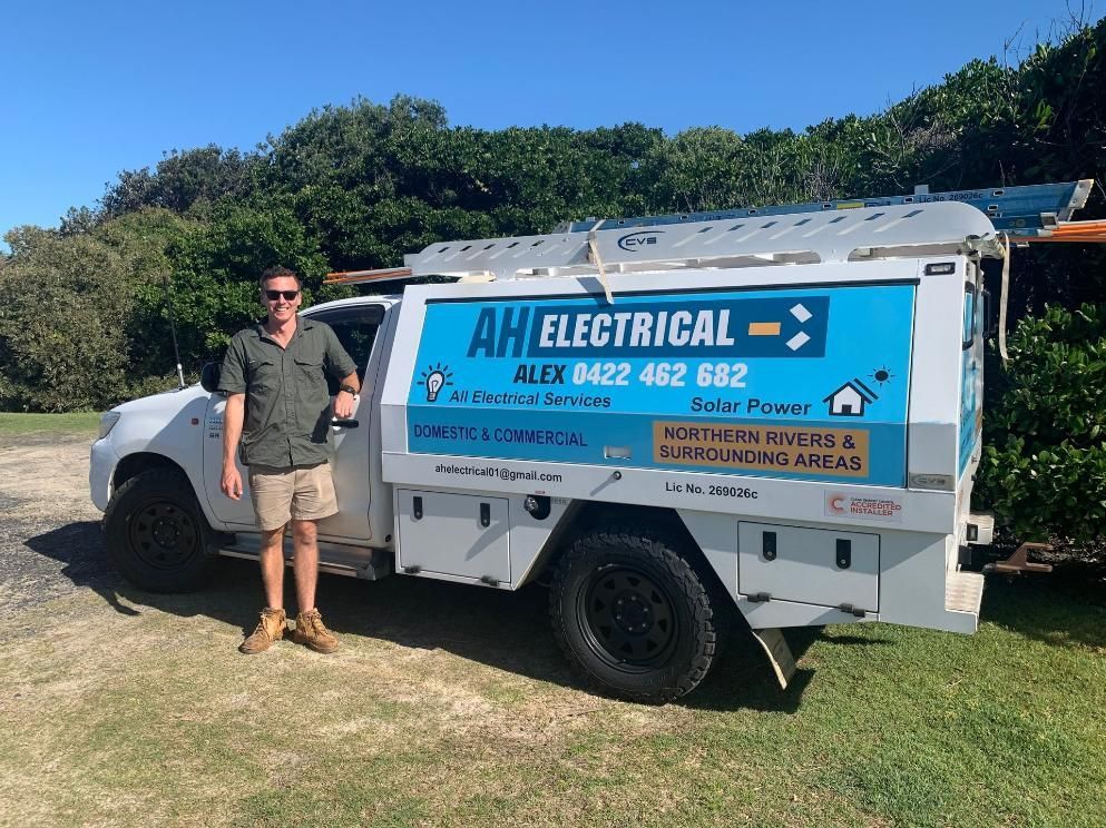 A Man Is Standing In Front Of An Electrical Truck — AH Electrical in Ballina, NSW