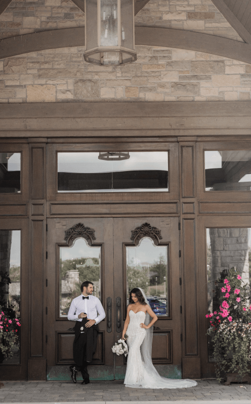 A married couple in front of the large wooden exterior doors to the Eagles Nest Golf Club Clubhouse.
