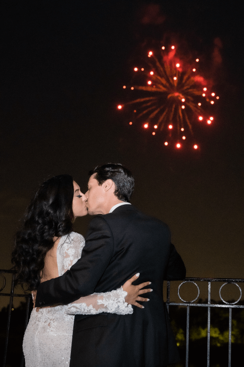 A bride and groom kissing in front of a fireworks display.