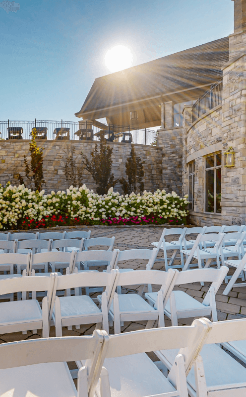 White chairs set up for a wedding ceremony on the lower patio, facing large white hydrangeas.