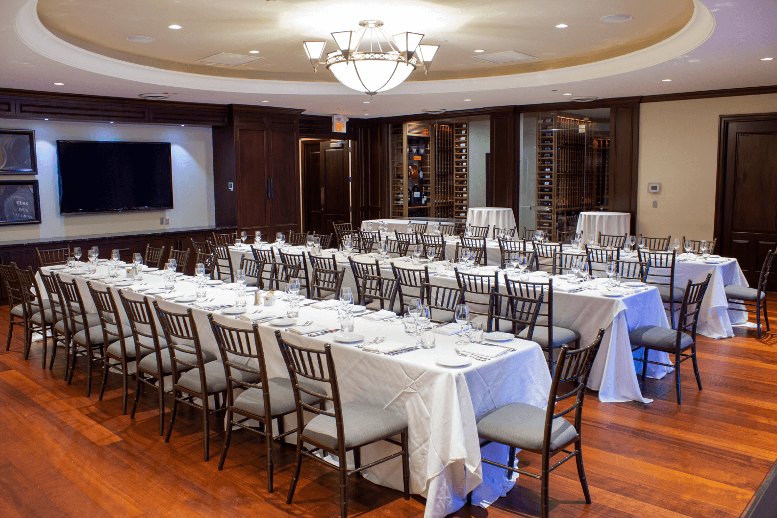 Three long tables set up in the Nest with a large TV hung on the wall and a wine cabinet.