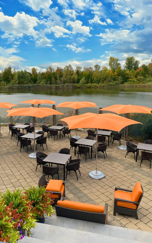The exterior of Jim & Garry's Pub. The patio with a view of the 18th hole pond and open orange table umbrellas.
