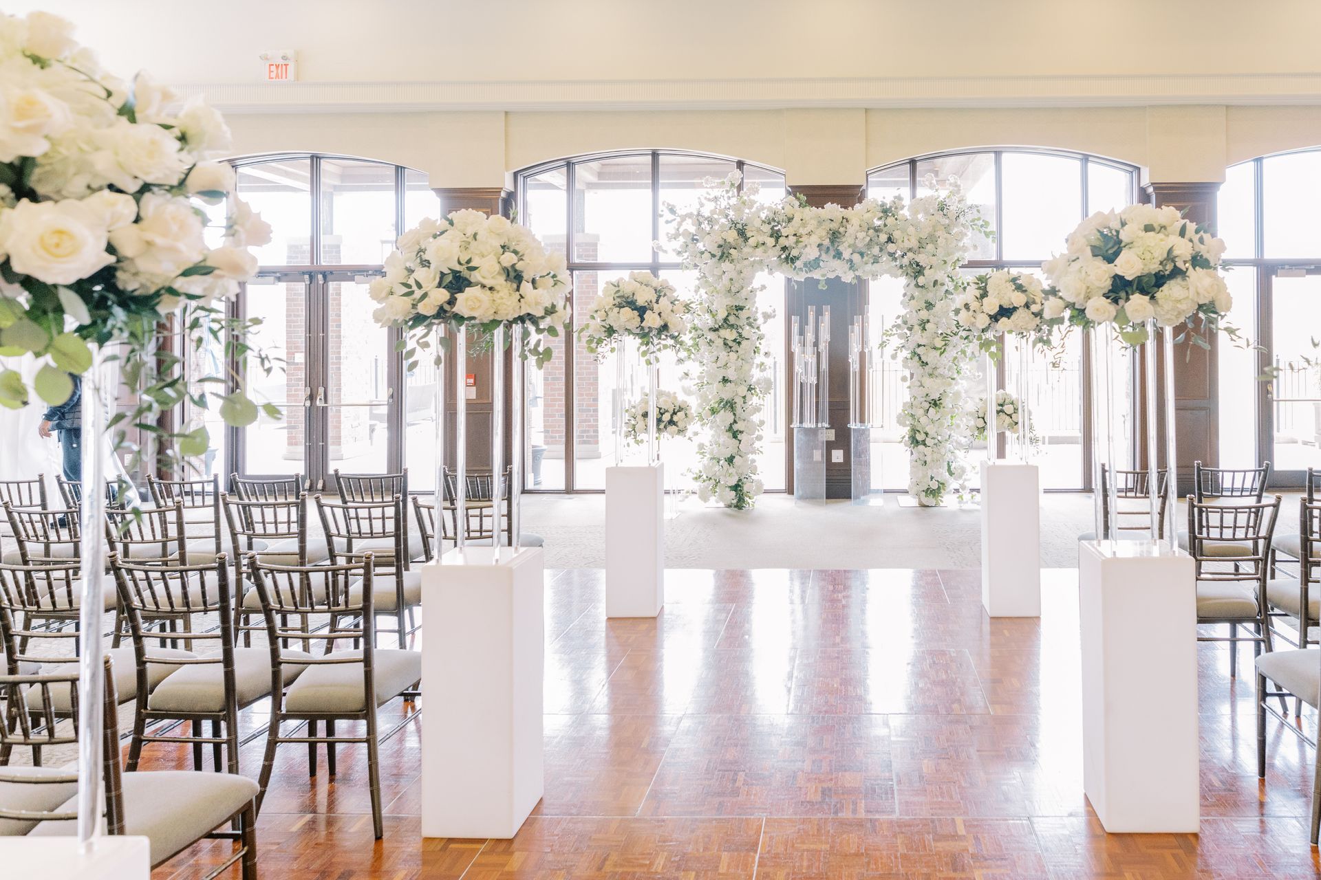 Indoor wedding ceremony in the Great Hall. Simple black chairs are facing large windows and surrounded by white flowers