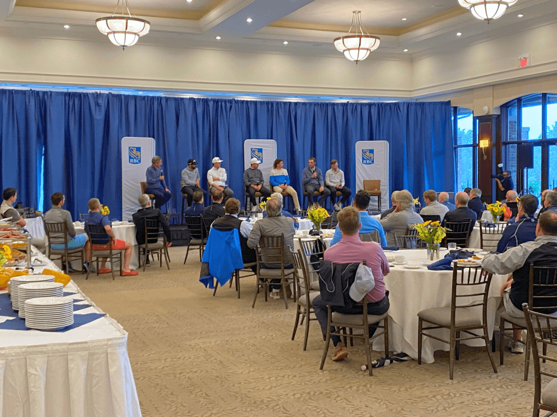 A large group of people sitting at tables in the Great Hall at Eagles Nest Golf Club. A blue curtain lines the perimeter