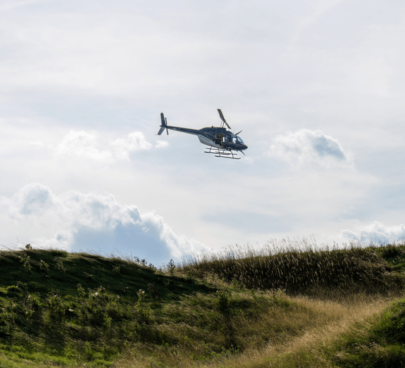 Helicopter flying over a grassy hill.