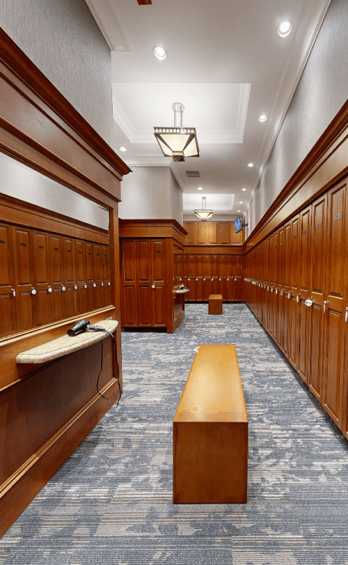 The men's locker room at Eagles Nest Golf Club with a blue carpet, wooden lockers, wooden benches, mirrors, and hair dryers.