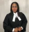 Lawyer in black robe with white neck tabs standing against a plain light backdrop