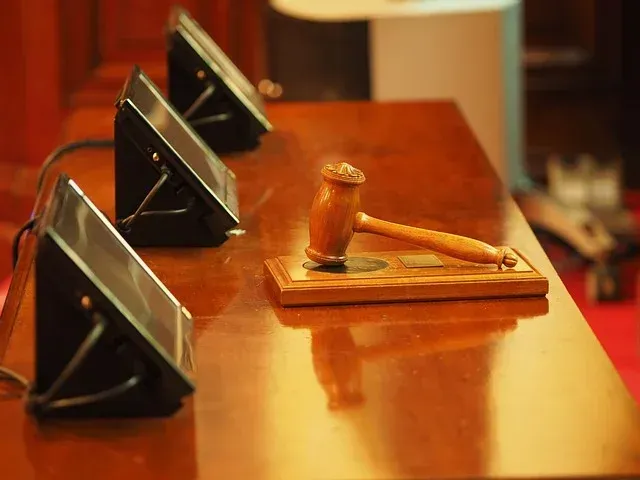 Wooden judge’s gavel on a bench with tablet stands in a courtroom, warmly lit.