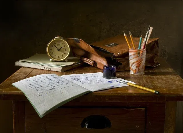 Desk with open notebook, clock, pencil cup, and scattered papers in warm light