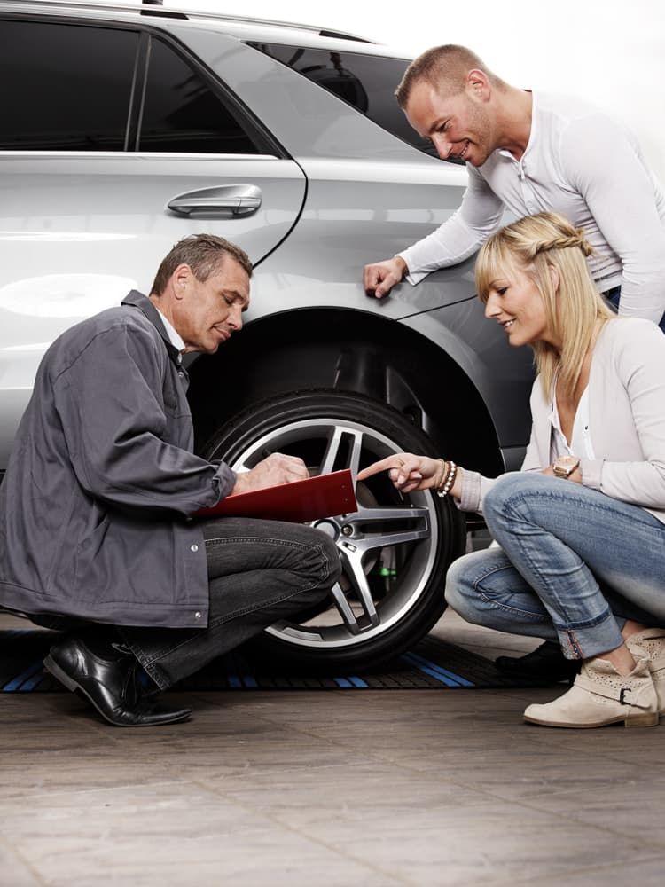 Auto Mechanic Shows a Couple a Car Tire Pointing at It While Writing — Autoplus Professionals Picton in Picton, NSW