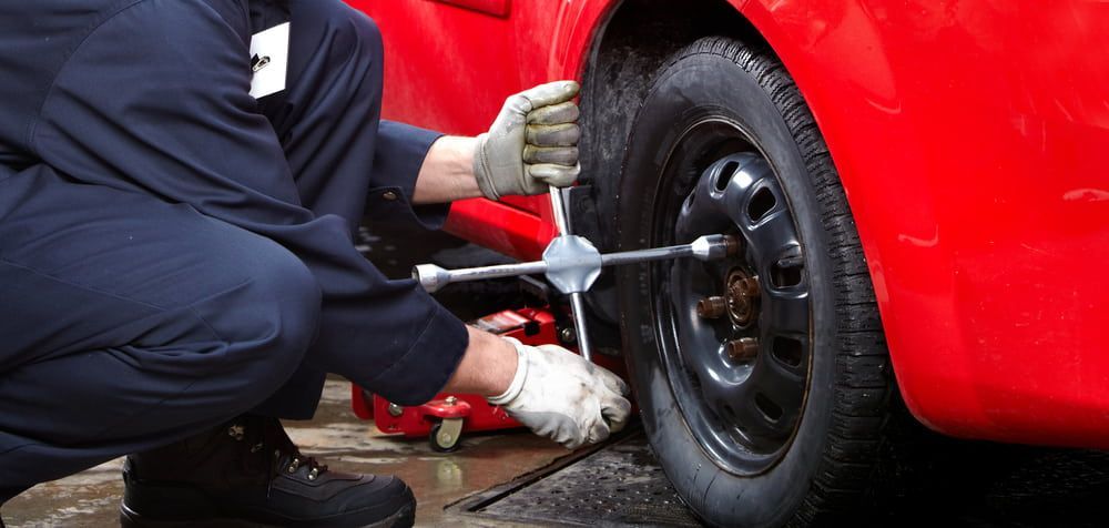 A Mechanic in Blue Overalls Changing a Tire on A Red Car — Autoplus Professionals Picton in Picton, NSW