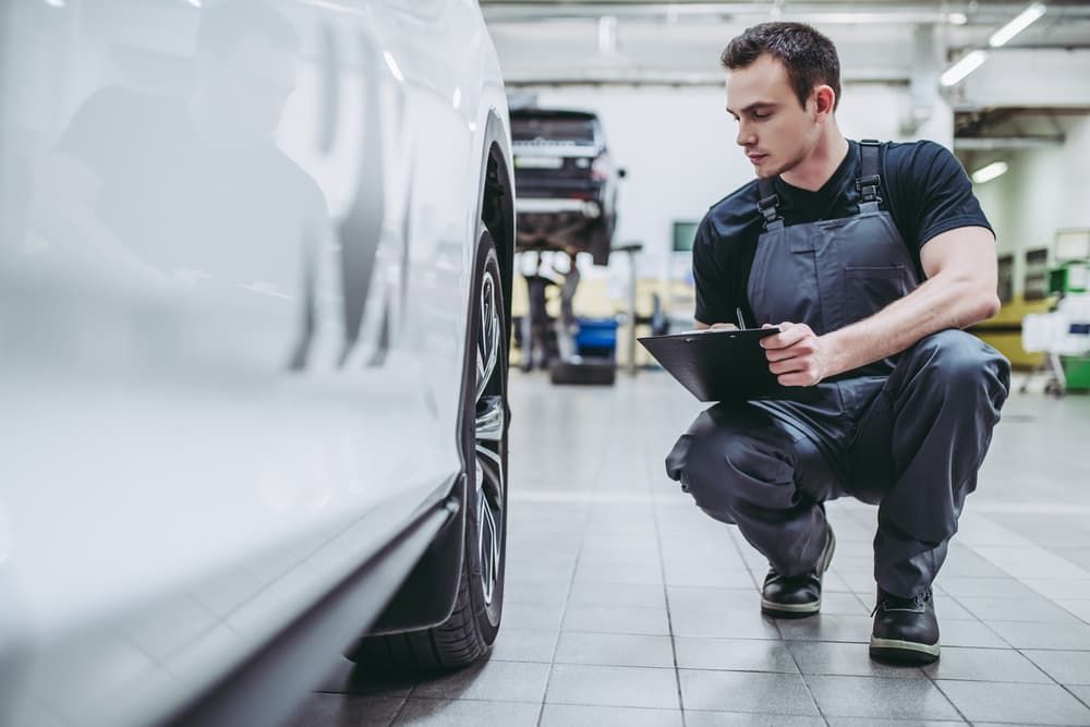 Mechanic in Grey Overalls Inspecting a Car Wheel with A Clipboard — Autoplus Professionals Picton in Picton, NSW