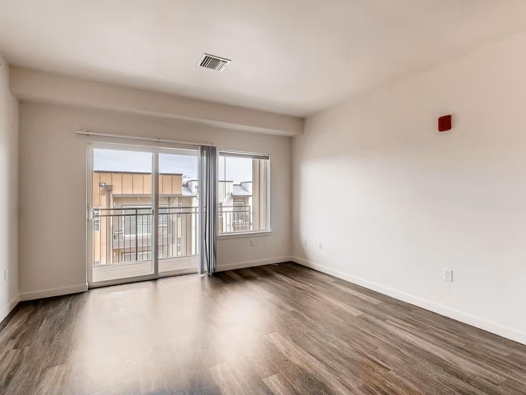 Empty room with wood-look flooring, white walls, and a large sliding glass door opening to a balcony.