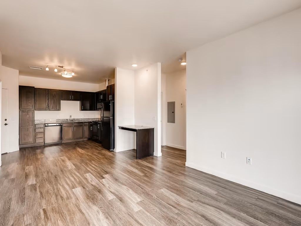 An open-concept living area with wood-look flooring and a kitchen featuring dark cabinets and stainless steel appliances.