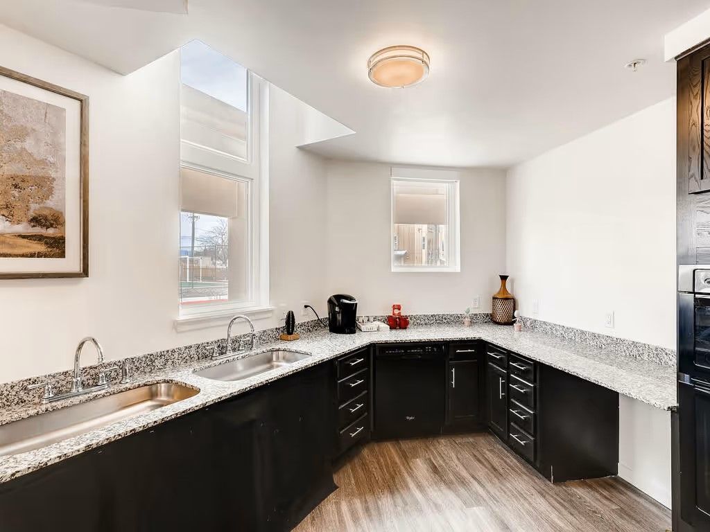 Modern kitchen with dark cabinets, granite countertops, stainless steel sink, and light wood flooring.