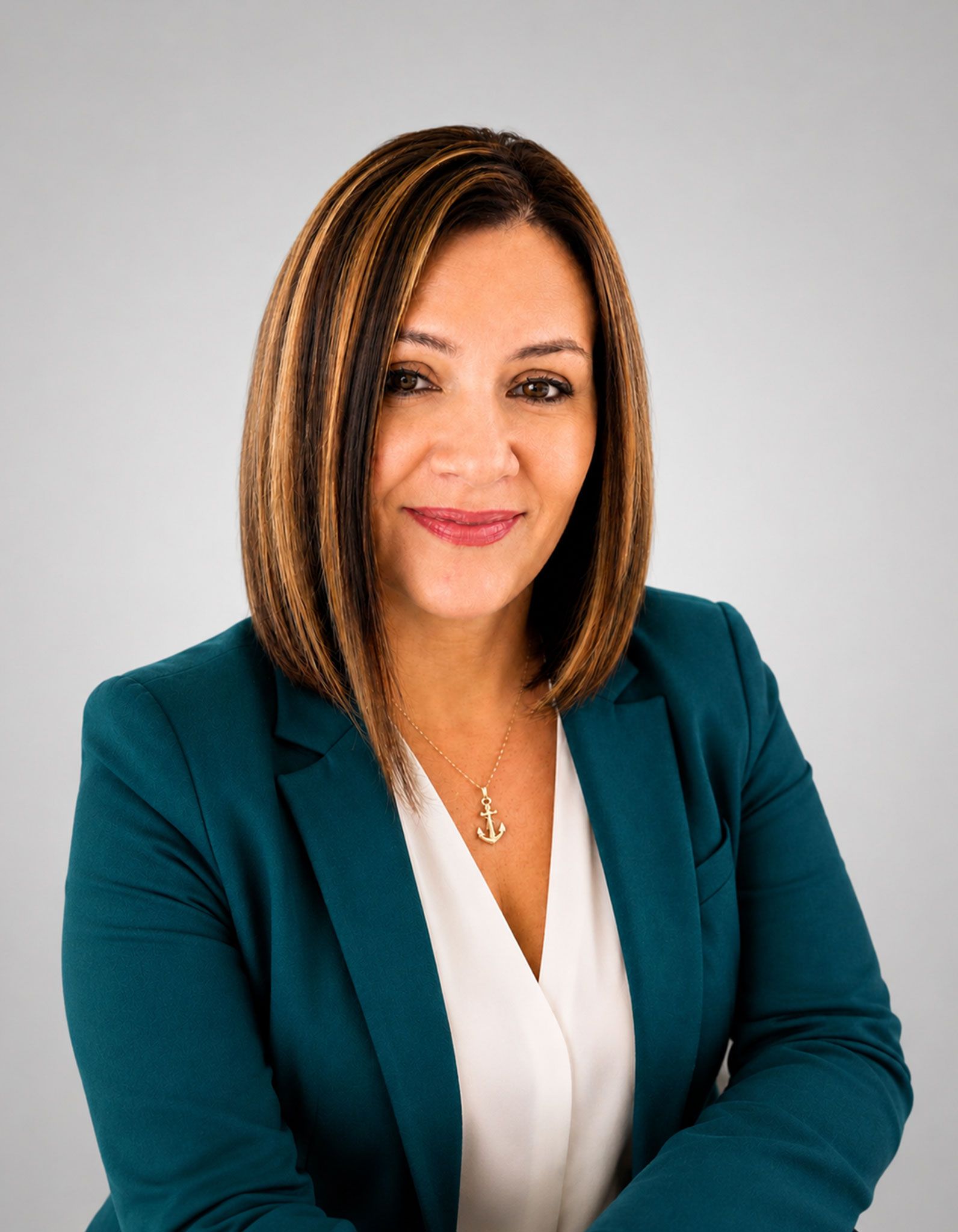 Professional headshot of a person in a teal blazer and white blouse against a gray background