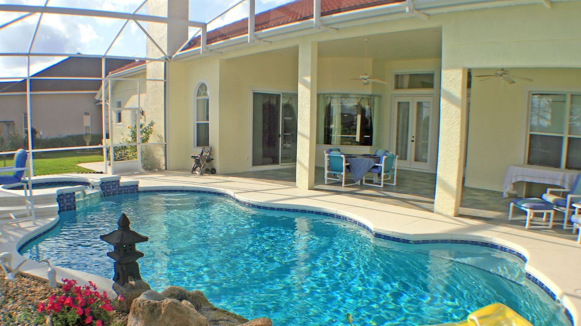 Backyard pool beside a beige house with patio chairs and screened enclosure