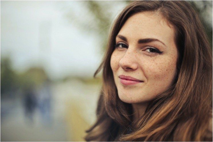 a woman with long brown hair and freckles is smiling for the camera .