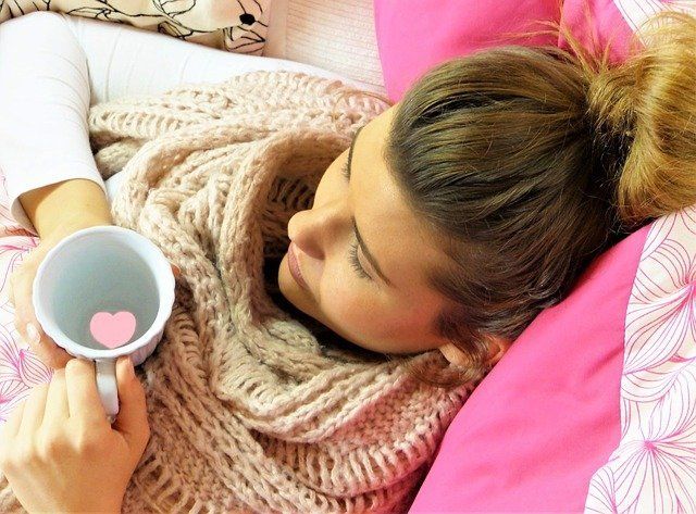 a woman is laying in bed holding a cup of coffee .