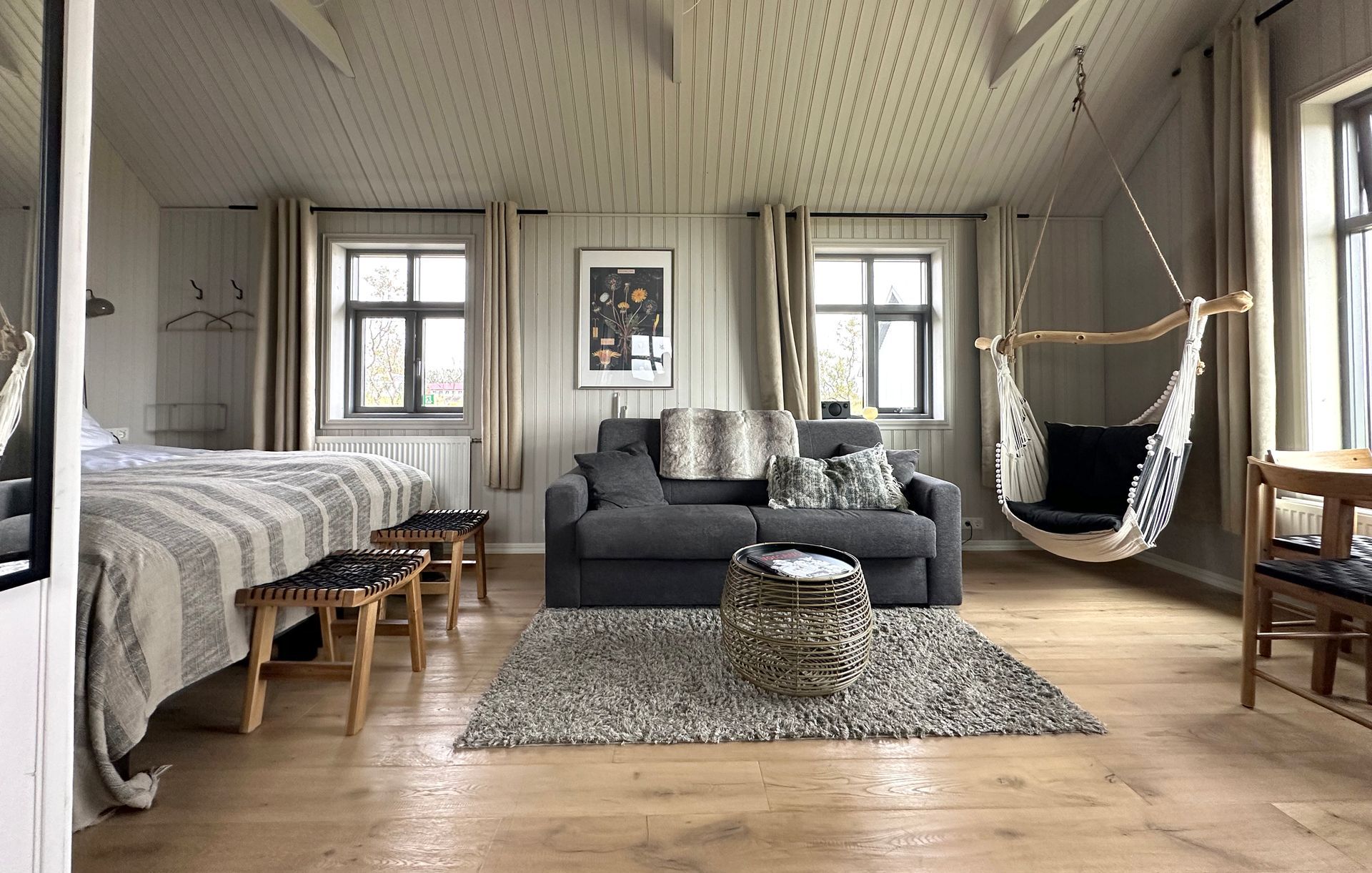A living room with a couch , chairs , and a hammock hanging from the ceiling.